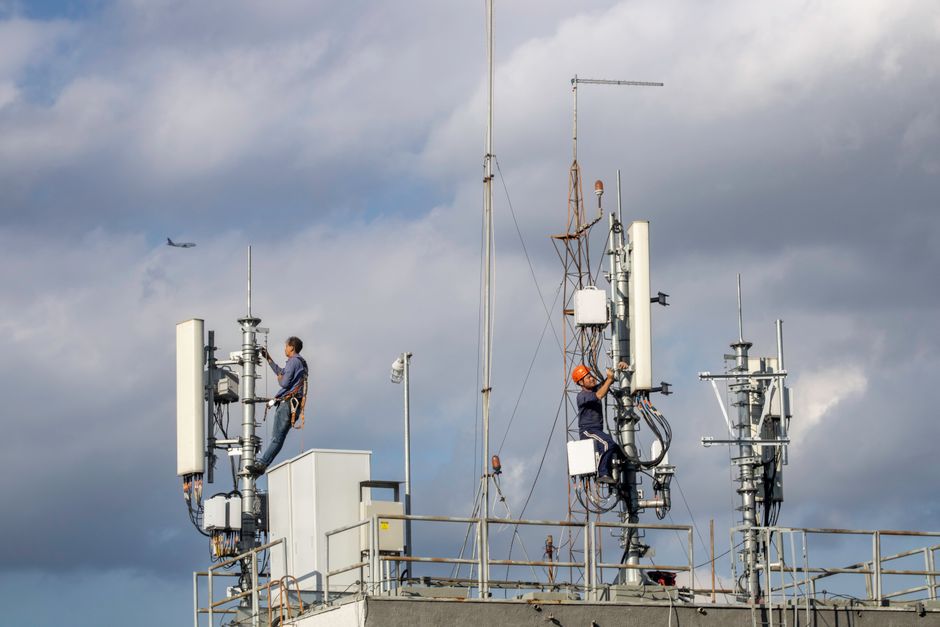 Technicy pracujący przy antenach nadawczych na dachu budynku pod zachmurzonym niebem