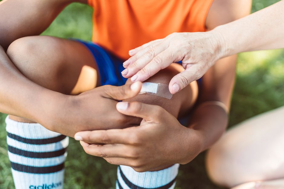 Dłoń naklejająca plaster na otarte kolano dziecka w stroju sportowym