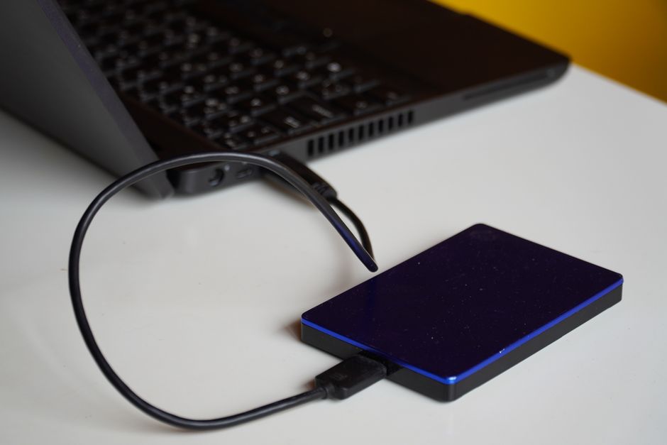 Zewnętrzny dysk twardy podłączony kablem USB do otwartego laptopa.