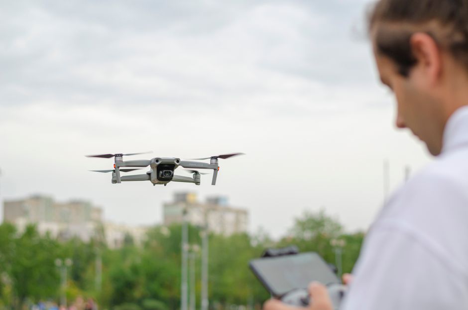 Mężczyzna sterujący dronem w otwartej przestrzeni miejskiej z zielenią w tle