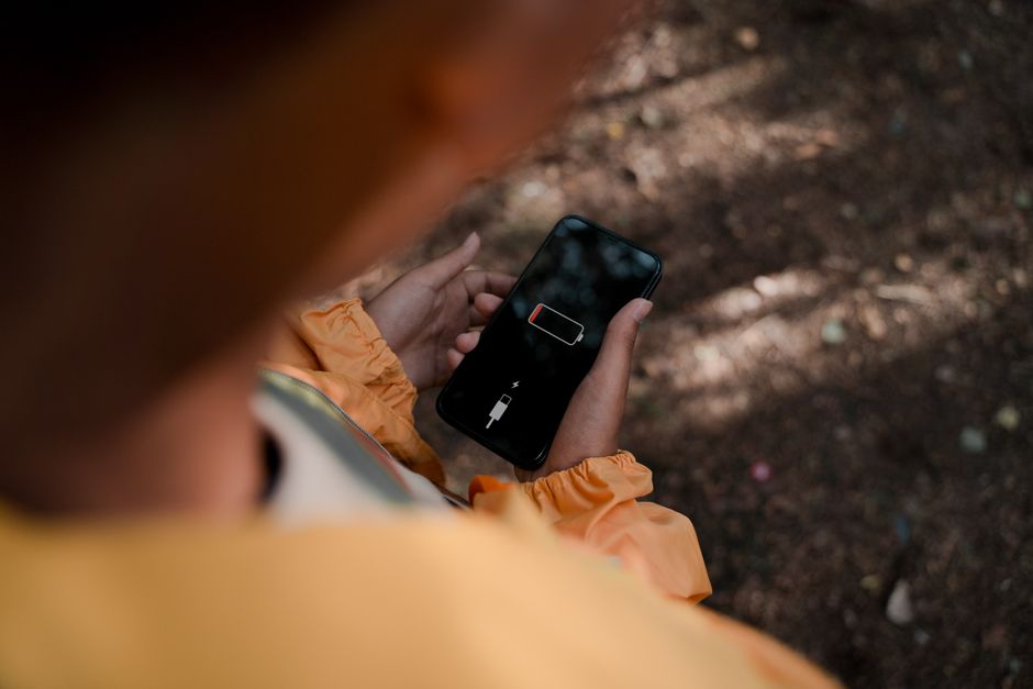 Osoba trzymająca smartfon z ikoną rozładowanej baterii na czarnym ekranie