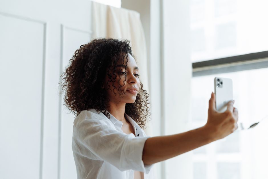Kobieta z kręconymi włosami robi selfie smartfonem w jasnym pomieszczeniu