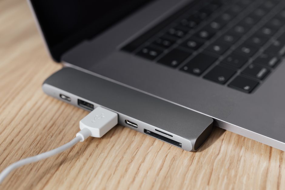 Szary hub USB podłączony do laptopa z wpiętym białym kablem