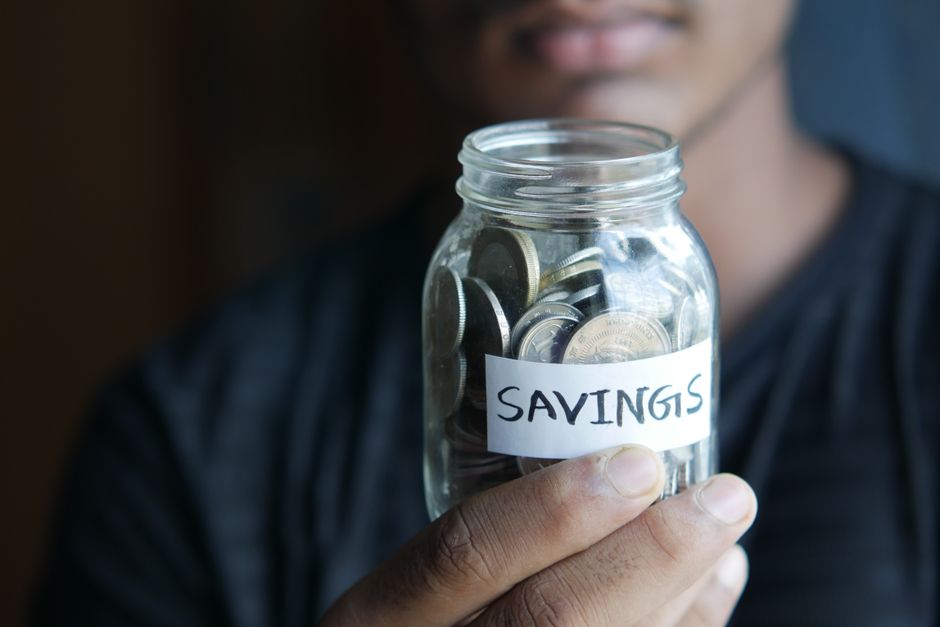 Dłoń trzymająca szklany słoik z monetami i etykietą z napisem Savings